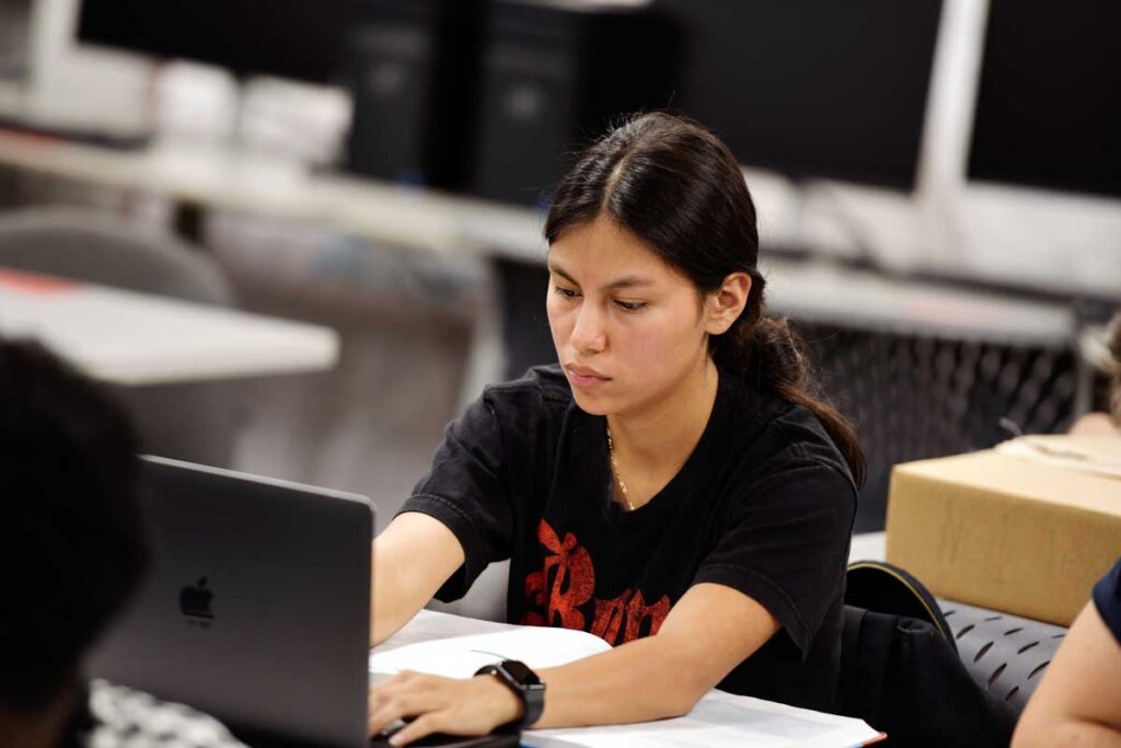 Photo of Maria typing on a laptop in a classroom.